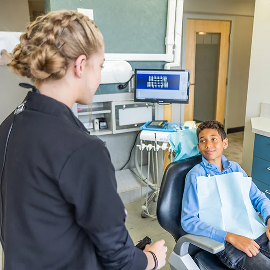 A hygienist talking with a young patient in the dental chair